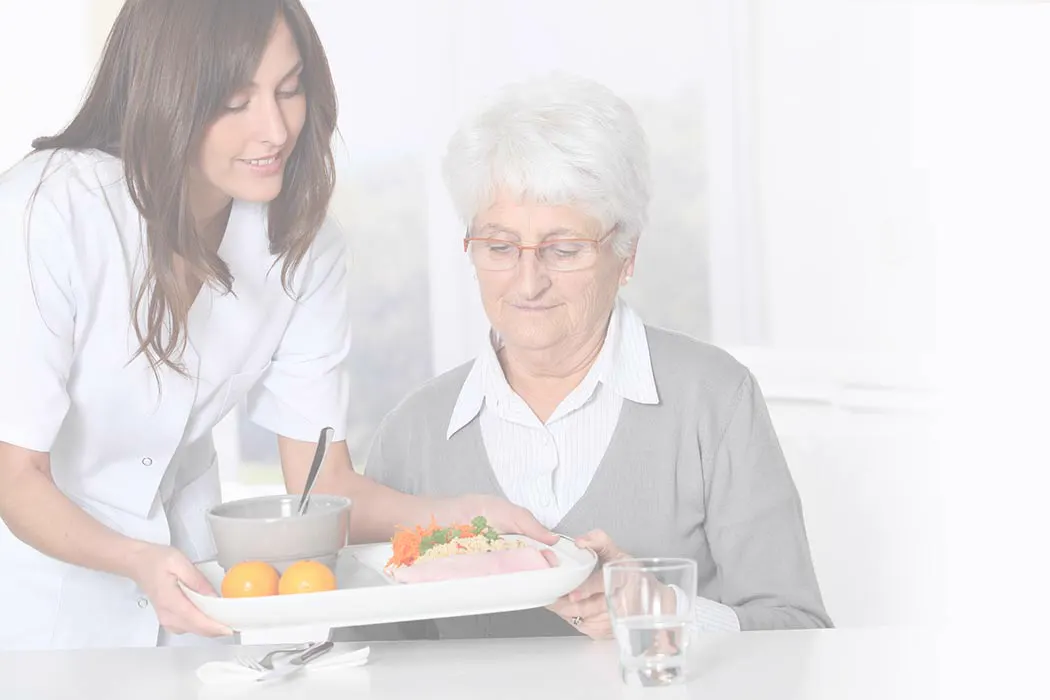 Caregiver serving meal to elderly woman